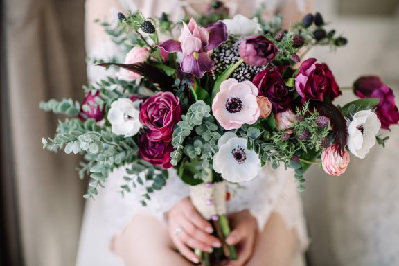 Bunte Blumenstrauß mit roten, weißen und lila Anemonen und grünem Laub.