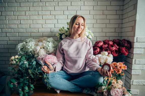 Frau sitzt lächelnd vor einem Blumenarrangement in verschiedenen Farben.